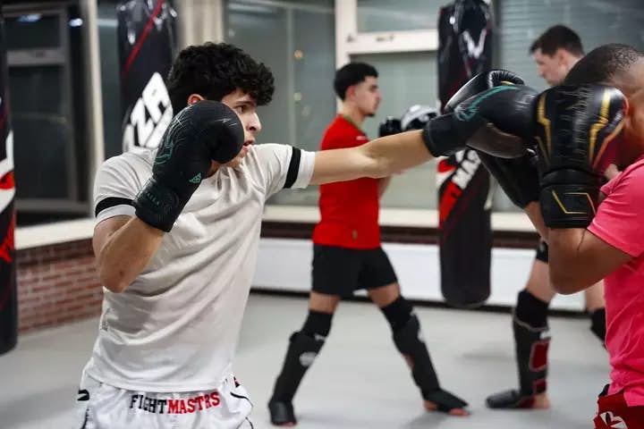 Een groep jonge mannen die kickboksen traint gezamenlijk kickboxing in een sportschool, waarbij ze hun kracht en vastberadenheid tonen.